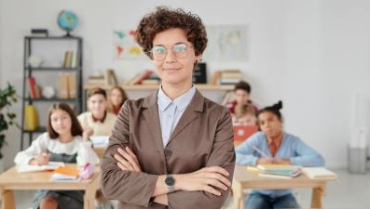 eine Lehrerin steht mit verschränkten Armen und mit dem Rücken zur Klasse. Symbolbild für das Thema: Recht im Schulzimmer. Was dürfen Lehrpersonen und was nicht?